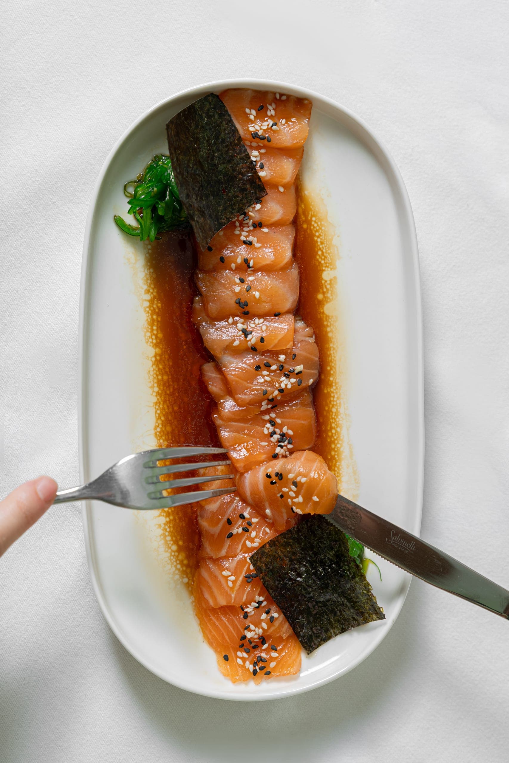 Sliced salmon sashimi with nori, sesame seeds and seaweed salad on a white platter